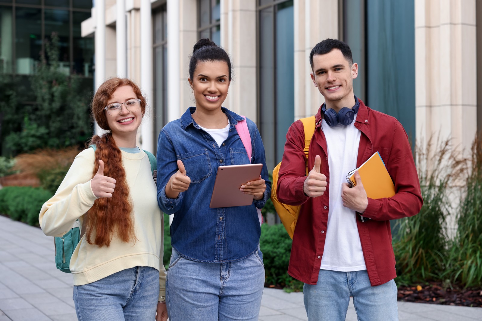 Photo of happy young students showing thumbs up outdoors