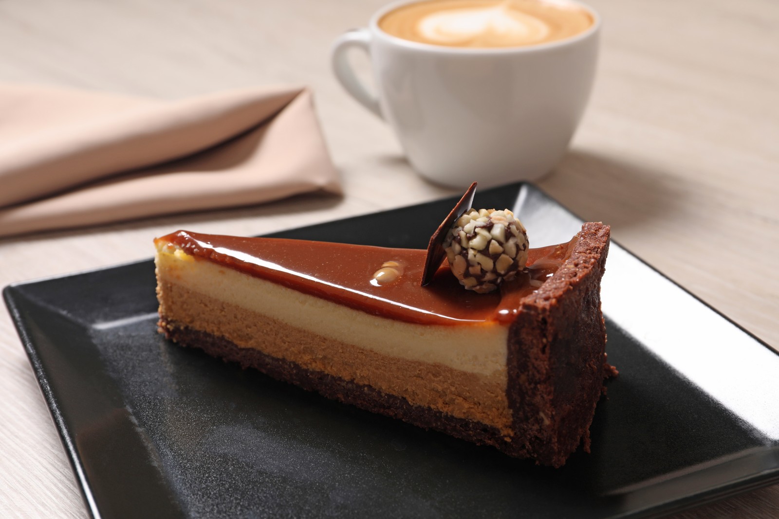 Photo of piece of delicious cheesecake with caramel and chocolate candy on table, closeup