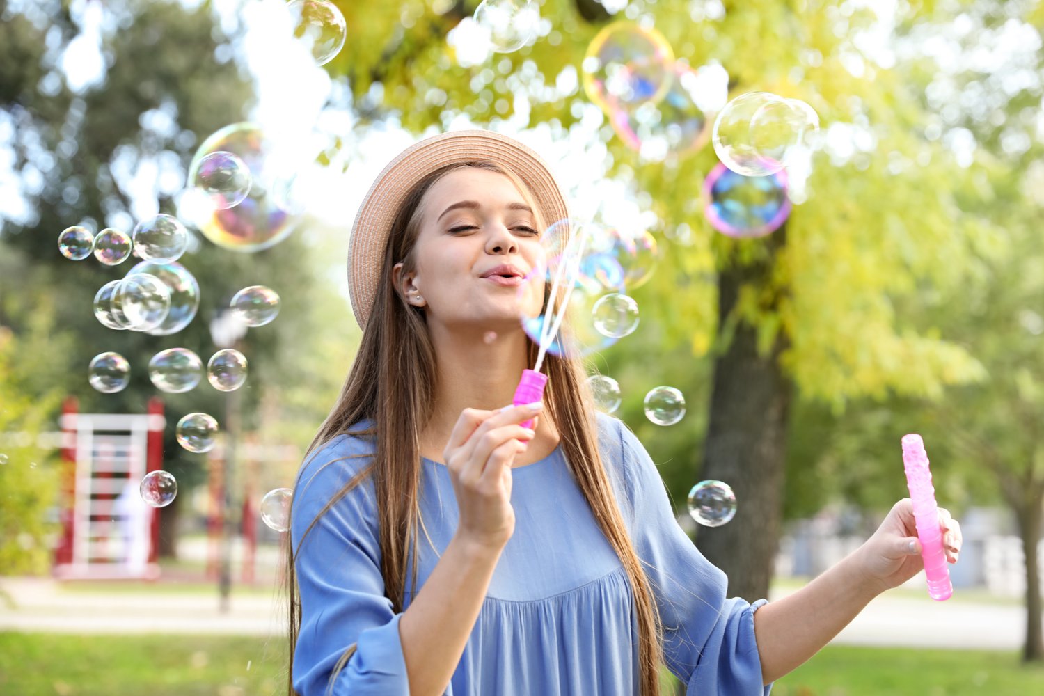 Photo of young woman blowing soap bubbles in park