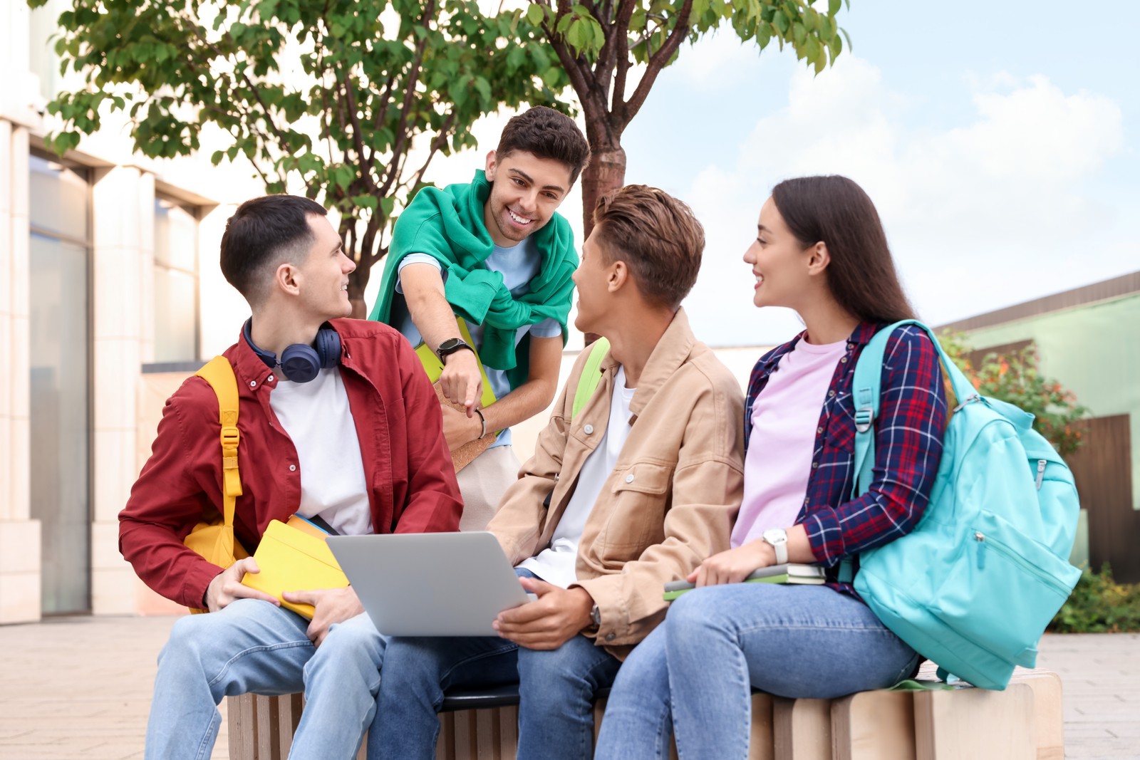Photo of group of happy young students with laptop learning together outdoors