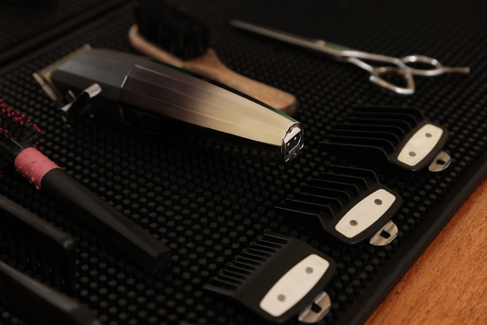 Photo of black rubber mat with hairdressing tools on wooden table, closeup