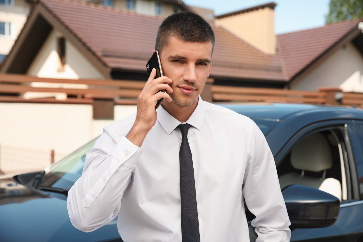 Photo of attractive young man talking on phone near luxury car outdoors