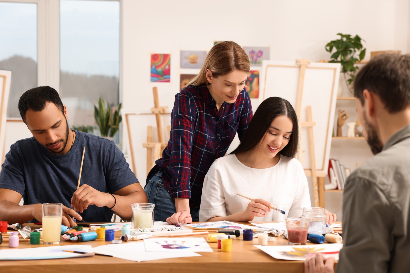 Photo of artist teaching her students to paint at table in studio. Creative hobby