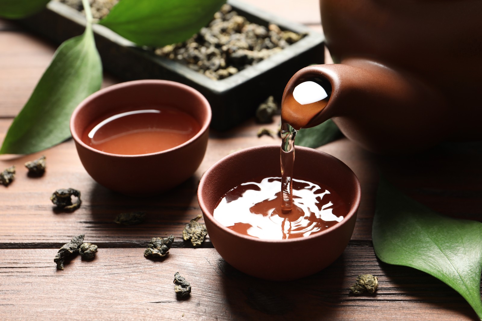 Photo of pouring Tie Guan Yin oolong tea into cup on wooden table