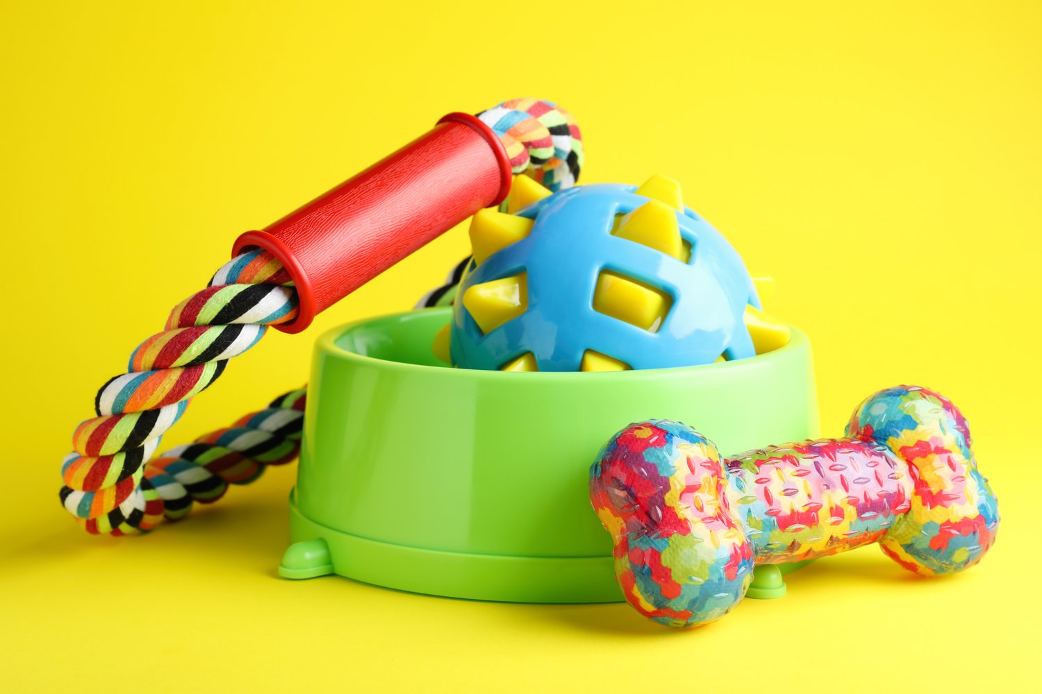 Photo of feeding bowl and toys for pet on yellow background
