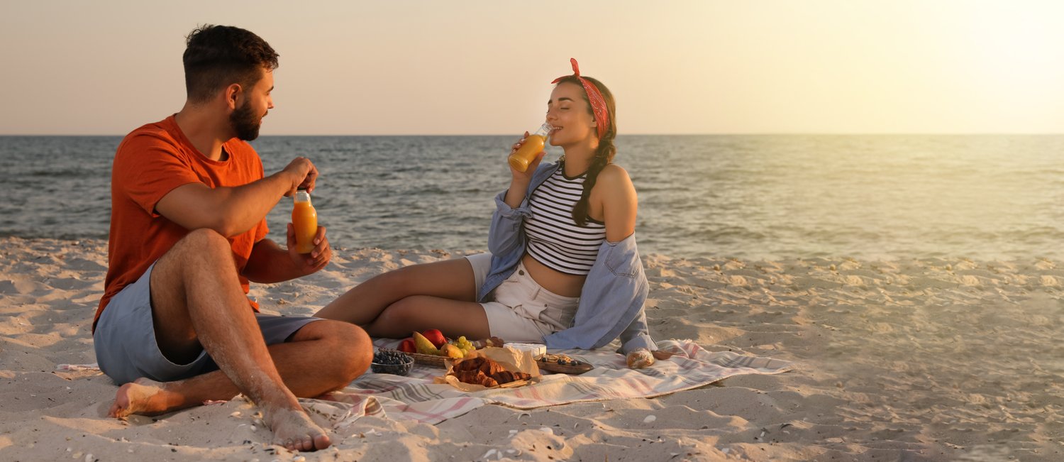 Photo of lovely couple having picnic on sandy beach near sea, space for text. Banner design