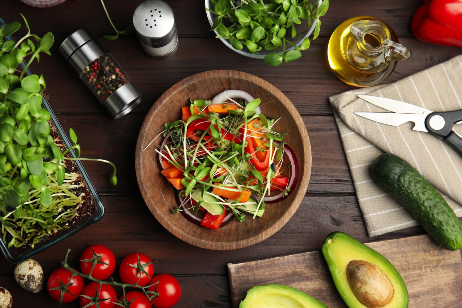 Photo of salad with fresh organic microgreen in bowl and ingredients on wooden table, flat lay