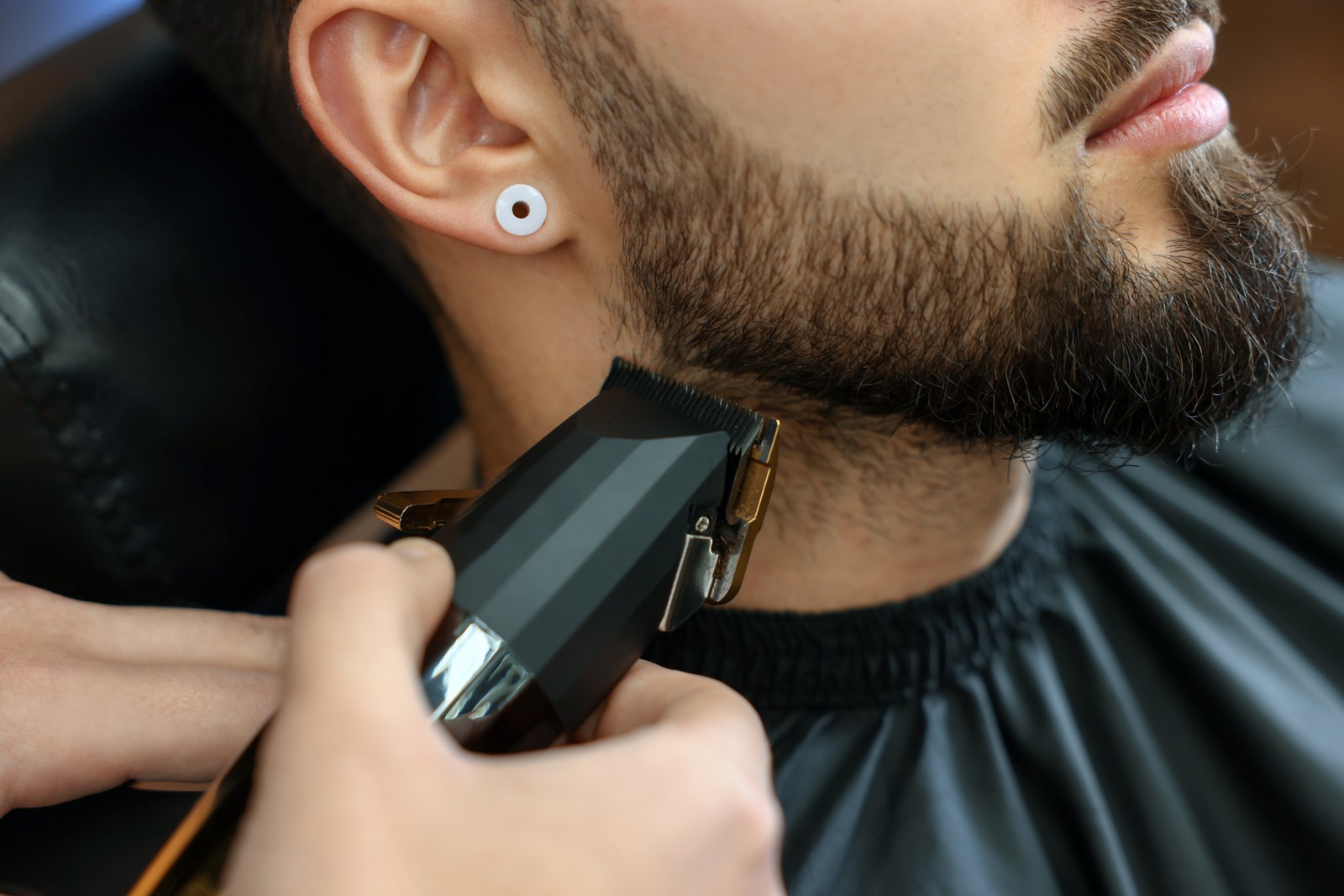 Photo of professional hairdresser working with bearded client in barbershop, closeup