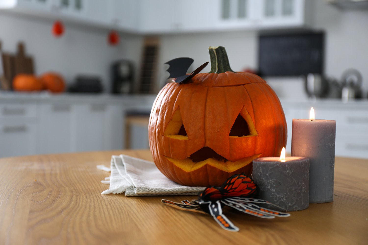 Photo of pumpkin jack o'lantern, candles and Halloween decor on wooden table in kitchen, space for text