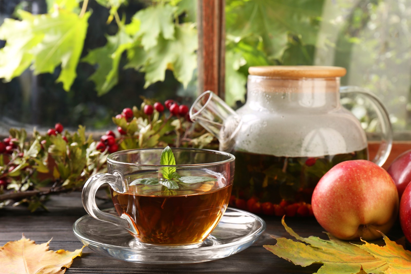 Photo of hot tea, apples and dry leaves on wooden windowsill. Autumn atmosphere