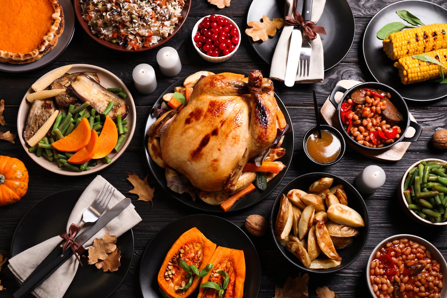 Photo of traditional Thanksgiving day feast with delicious cooked turkey and other seasonal dishes served on black wooden table, flat lay