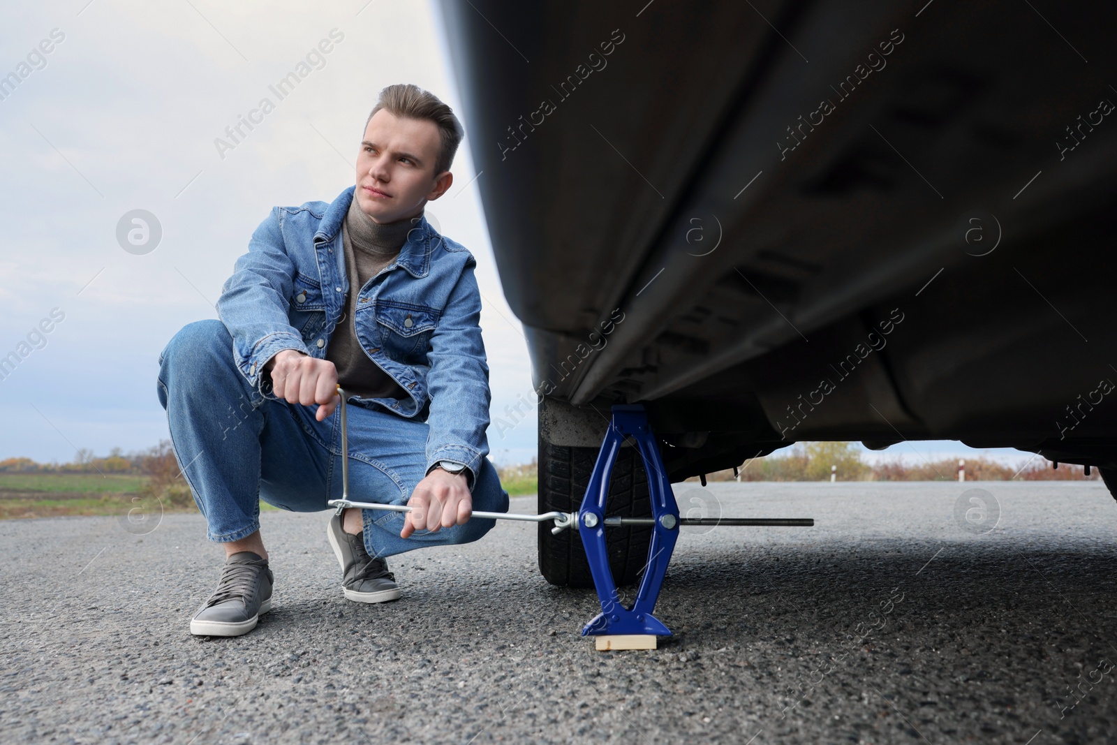 Photo of Young man changing tire of car on roadside