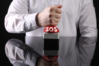 Image of Man pressing red SOS button at black table, closeup