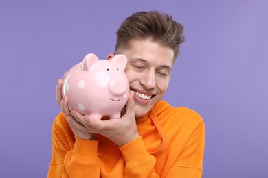 Photo of Happy man with piggy bank on purple background