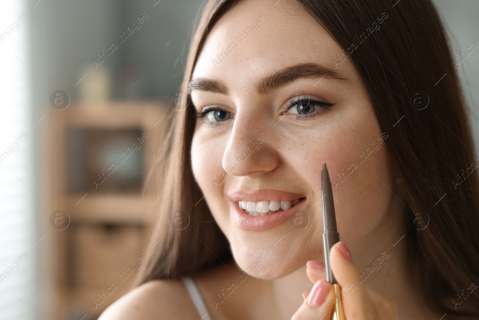 Photo of Smiling woman drawing freckles with pen indoors