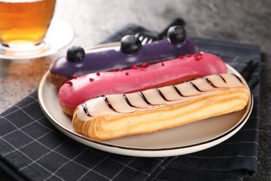 Plate with different tasty glazed eclairs on table, closeup