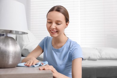 Photo of Woman with microfiber cloth cleaning wooden chest of drawers in room