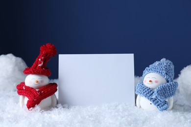 Photo of Cute decorative snowmen and blank card on snow against blue background