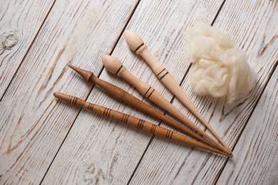 Photo of Soft wool and spindles on white wooden table, flat lay