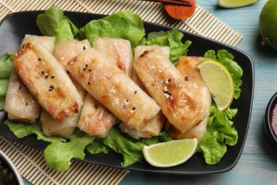 Photo of Tasty fried spring rolls, lettuce and lime on light blue wooden table, top view