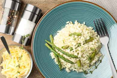 Photo of Delicious risotto with asparagus served on wooden table, flat lay