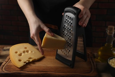 Photo of Woman grating cheese at wooden table, closeup