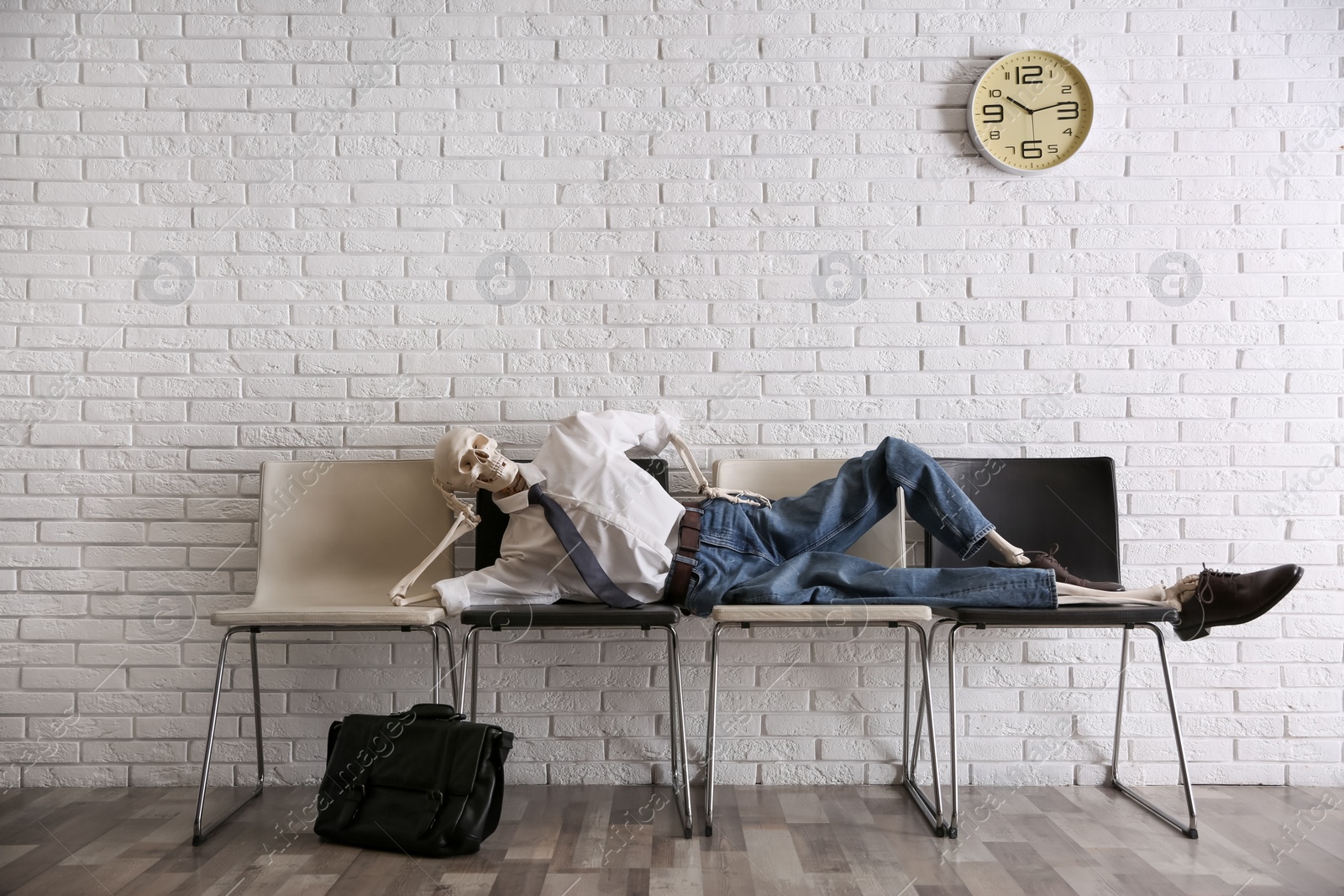 Human skeleton in office wear lying on chairs near brick wall indoors Photo of Human skeleton in office wear lying on chairs near brick wall indoors