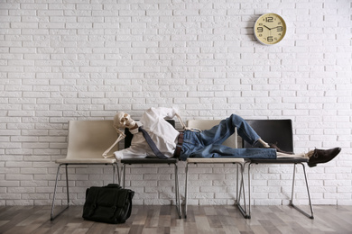 Photo of Human skeleton in office wear lying on chairs near brick wall indoors