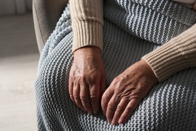 Photo of Elderly woman with knitted blanket indoors, closeup