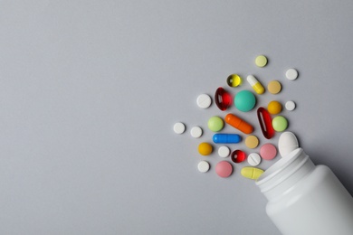Photo of Bottle with different pills on grey background, flat lay. Space for text