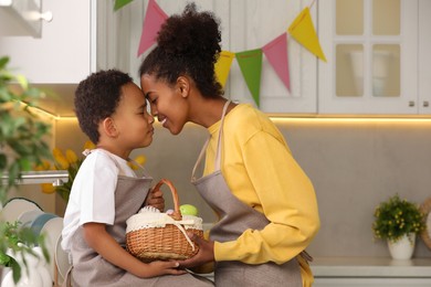 Photo of Happy African American mother and her cute son with Easter eggs touching foreheads in kitchen