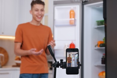 Photo of Food blogger recording video in kitchen, focus on smartphone