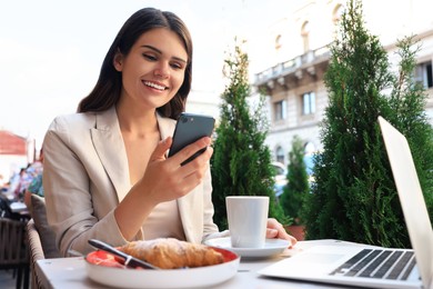 Beautiful young woman using smartphone in outdoor cafe