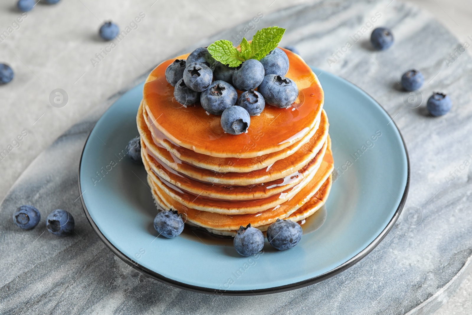 Photo of Plate of delicious pancakes with fresh blueberries and syrup on grey table
