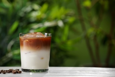 Photo of Glass of iced coffee and beans on white wooden table outdoors. Space for text