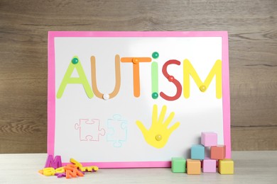 Photo of Magnetic board with word Autism and toys on white wooden table