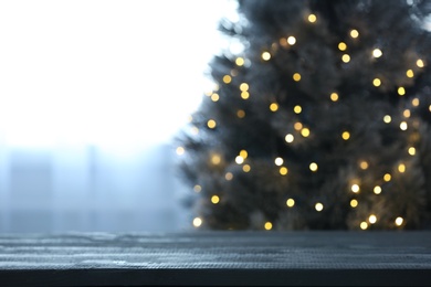 Photo of Blurred view of beautiful Christmas tree with yellow lights near window indoors, focus on wooden table. Space for text