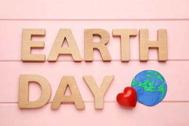 Photo of Words Earth Day, plasticine planet and decorative heart on pink wooden table, flat lay