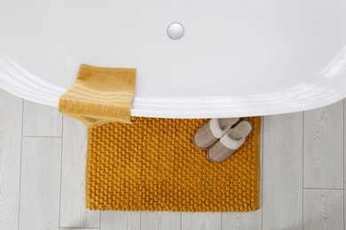 Photo of Soft orange bath mat and slippers on floor in bathroom, top view