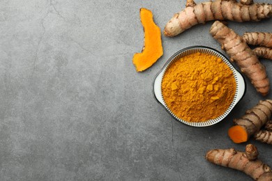 Photo of Bowl with turmeric powder and raw roots on grey table, flat lay. Space for text