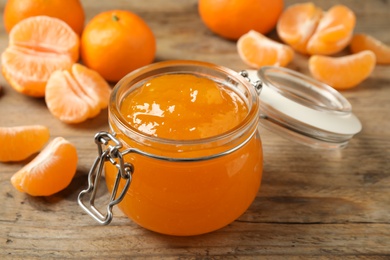 Photo of Tasty tangerine jam in glass jar on wooden table