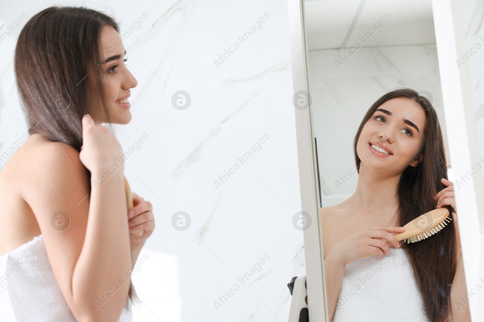 Beautiful young woman with hair brush looking into mirror in bathroom Photo of Beautiful young woman with hair brush looking into mirror in bathroom