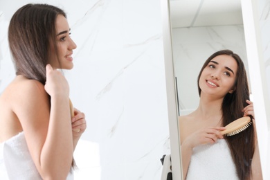 Photo of Beautiful young woman with hair brush looking into mirror in bathroom