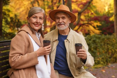 Photo of Affectionate senior couple with cups of coffee spending time together on bench in autumn park
