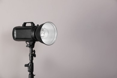 Photo of Professional studio flash light with reflector on tripod against grey background, space for text. Photography equipment