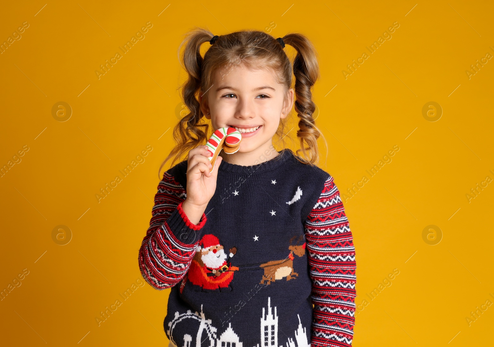 Photo of Cute little girl with Christmas gingerbread cookie on yellow background