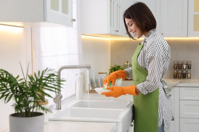 Photo of Happy young woman washing plate above sink in modern kitchen