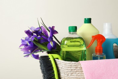 Photo of Spring cleaning. Wicker basket with detergents, flowers and tools on yellow background, closeup