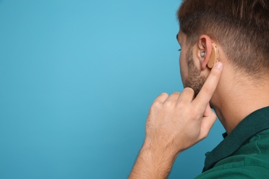 Photo of Young man adjusting hearing aid on color background. Space for text