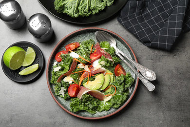 Photo of Delicious kale salad with prosciutto served on grey table, flat lay